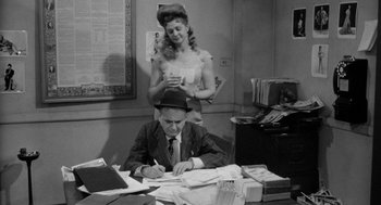 Movie still from “Mickey One” (1965), directed by Arthur Penn – A woman standing next to a man sitting at a desk; Medium shot, High angle