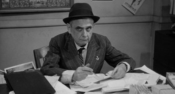 Movie still from “Mickey One” (1965), directed by Arthur Penn – An older man sitting at a table writing on papers; Medium shot, Over the shoulder angle