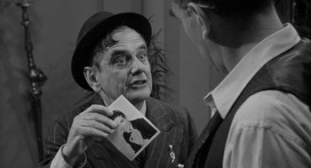 Movie still from “Mickey One” (1965), directed by Arthur Penn – A man in a suit and a hat holding a picture; Close Up shot, Over the shoulder angle