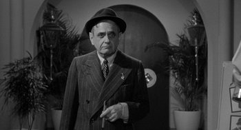 Movie still from “Mickey One” (1965), directed by Arthur Penn – An older man wearing a suit and hat holding a cigarette; Medium shot, Low angle