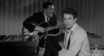 Movie still from “Mickey One” (1965), directed by Arthur Penn – A man playing a guitar while another man looks on; Medium shot, Low angle
