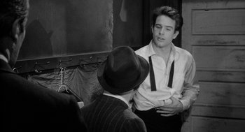 Movie still from “Mickey One” (1965), directed by Arthur Penn – A man wearing a hat and a tie talking to another man in a suit; Medium shot, Over the shoulder angle