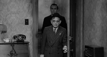 Movie still from “Mickey One” (1965), directed by Arthur Penn – A man in a suit and tie standing next to another man in a suit and tie; Medium shot, Over the shoulder angle