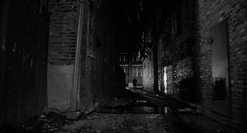 Movie still from “Mickey One” (1965), directed by Arthur Penn – A person is walking down a dark alley way at night; Extreme Wide shot, High angle