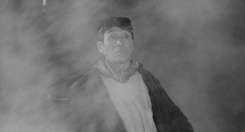 Movie still from “Mickey One” (1965), directed by Arthur Penn – A man in a hat and a jacket is in the fog; Medium shot, Low angle