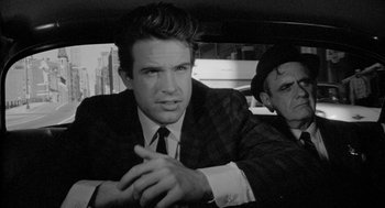 Movie still from “Mickey One” (1965), directed by Arthur Penn – A man in a suit sitting next to another man in a hat; Close Up shot, Over the shoulder angle