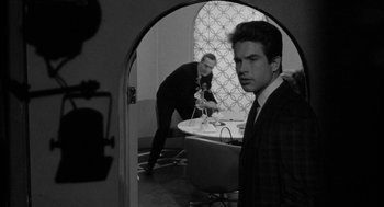 Movie still from “Mickey One” (1965), directed by Arthur Penn – A man in a suit and tie standing in front of a table; Medium shot, Over the shoulder angle