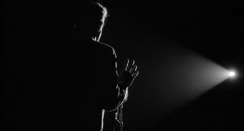 Movie still from “Mickey One” (1965), directed by Arthur Penn – A man standing in the dark holding a microphone; Medium shot, Low angle