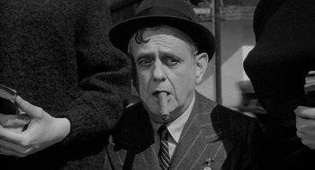 Movie still from “Mickey One” (1965), directed by Arthur Penn – An older man wearing a suit and hat smoking a cigarette; Close Up shot, Over the shoulder angle