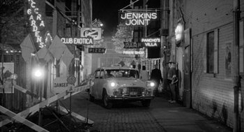 Movie still from “Mickey One” (1965), directed by Arthur Penn – An old car driving down a street at night; Wide shot, High angle