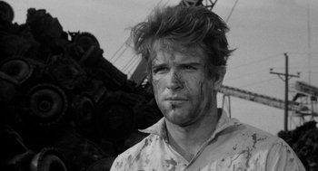 Movie still from “Mickey One” (1965), directed by Arthur Penn – Black and white photograph of a man with mud all over his face; Close Up shot, Over the shoulder angle