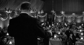 Movie still from “Mickey One” (1965), directed by Arthur Penn – A group of people sitting in a room with candles; Wide shot, Over the shoulder angle