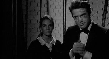 Movie still from “Mickey One” (1965), directed by Arthur Penn – A man and a woman standing next to each other in front of a brick wall; Medium shot, Low angle