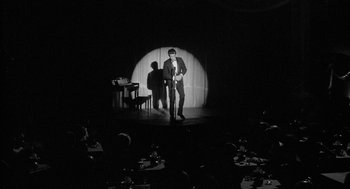 Movie still from “Mickey One” (1965), directed by Arthur Penn – A black and white photo of a man on a stage; Wide shot, High angle