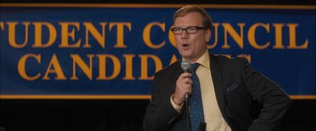 Movie still from “Middle School: The Worst Years of My Life” (2016), directed by Steve Carr – A man in a suit and tie holding a microphone; Medium shot, High angle