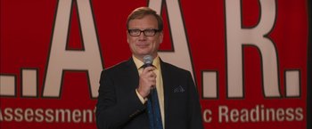 Movie still from “Middle School: The Worst Years of My Life” (2016), directed by Steve Carr – A man holding a microphone while standing in front of a red wall; Close Up shot, Over the shoulder angle
