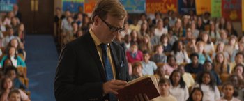 Movie still from “Middle School: The Worst Years of My Life” (2016), directed by Steve Carr – A man reading a book in front of an audience; Medium shot, Low angle