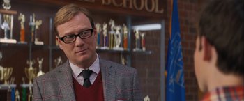 Movie still from “Middle School: The Worst Years of My Life” (2016), directed by Steve Carr – A man in a suit and tie standing in front of trophies; Close Up shot, Over the shoulder angle