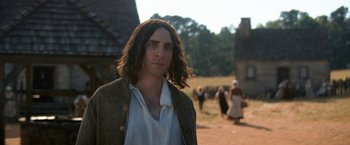 Movie still from “Fear Street: Part Three - 1666” (2021), directed by Leigh Janiak – A man with long brown hair standing in a field; Medium shot, Low angle