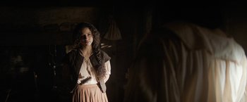 Movie still from “Fear Street: Part Three - 1666” (2021), directed by Leigh Janiak – A young woman standing in a dimly - lit room; Medium shot, Over the shoulder angle