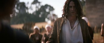 Movie still from “Fear Street: Part Three - 1666” (2021), directed by Leigh Janiak – A man with long curly hair standing in front of two other men; Medium shot, Over the shoulder angle