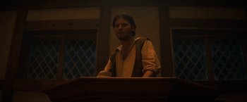 Movie still from “Fear Street: Part Three - 1666” (2021), directed by Leigh Janiak – A man standing at a podium in front of a window; Medium shot, Low angle