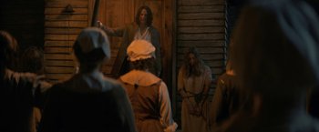 Movie still from “Fear Street: Part Three - 1666” (2021), directed by Leigh Janiak – A group of people standing in front of a wooden wall; Wide shot, Over the shoulder angle