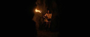 Movie still from “Fear Street: Part Three - 1666” (2021), directed by Leigh Janiak – A man holding a flaming stick in a cave; Wide shot, High angle