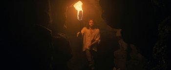 Movie still from “Fear Street: Part Three - 1666” (2021), directed by Leigh Janiak – A bearded man holding a torch in a cave; Medium shot, Low angle