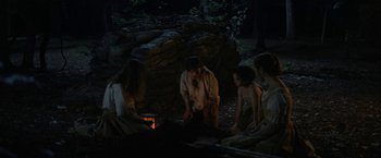 Movie still from “Fear Street: Part Three - 1666” (2021), directed by Leigh Janiak – A group of people gathered around a fire in the woods; Wide shot, High angle