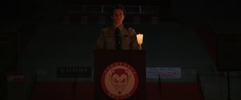 Movie still from “Fear Street: Part Three - 1666” (2021), directed by Leigh Janiak – A man standing at a podium in front of a building; Medium shot, Low angle