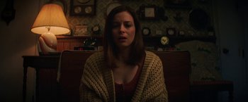 Movie still from “Fear Street: Part Three - 1666” (2021), directed by Leigh Janiak – A woman sitting in front of a wall with clocks on the wall; Medium shot, Over the shoulder angle