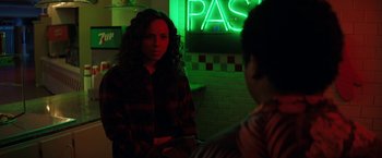 Movie still from “Fear Street: Part Three - 1666” (2021), directed by Leigh Janiak – A woman is sitting in front of a neon sign; Medium shot, Over the shoulder angle