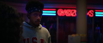 Movie still from “Fear Street: Part Three - 1666” (2021), directed by Leigh Janiak – A man in a hat is standing in front of a neon sign; Close Up shot, Low angle