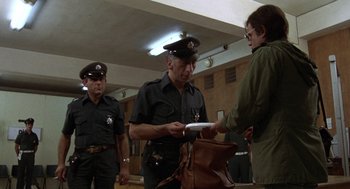 Movie still from “Midnight Express” (1978), directed by Alan Parker – A group of men standing next to each other in a room; Medium shot, Over the shoulder angle