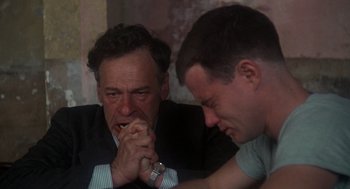 Movie still from “Midnight Express” (1978), directed by Alan Parker – Two men sitting at a table with their hands touching each other; Close Up shot, Over the shoulder angle