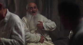 Movie still from “Midnight Express” (1978), directed by Alan Parker – An old man with a long white beard is sitting down; Medium shot, Over the shoulder angle