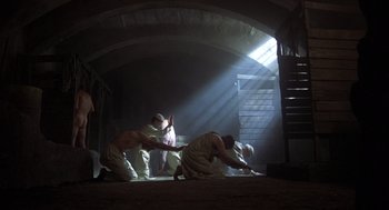 Movie still from “Midnight Express” (1978), directed by Alan Parker – A group of men kneeling on the ground under a beam of light; Wide shot, High angle