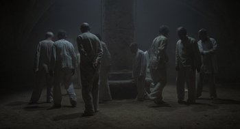 Movie still from “Midnight Express” (1978), directed by Alan Parker – A group of men standing around a pillar in the dark; Wide shot, High angle