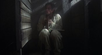 Movie still from “Midnight Express” (1978), directed by Alan Parker – A man sitting in a dark room holding a knife; Wide shot, High angle