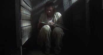 Movie still from “Midnight Express” (1978), directed by Alan Parker – A man sitting on the ground reading a book; Wide shot, High angle