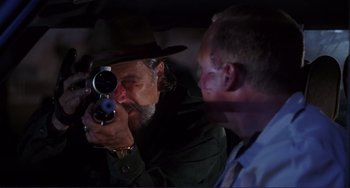 Movie still from “Mighty Joe Young” (1998), directed by Ron Underwood – A man in a hat is taking a picture of another man in a car; Medium shot, Over the shoulder angle