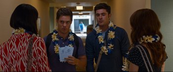 Movie still from “Mike and Dave Need Wedding Dates” (2016), directed by Jake Szymanski – Two young men wearing leis standing next to each other in a hallway; Medium shot, Over the shoulder angle