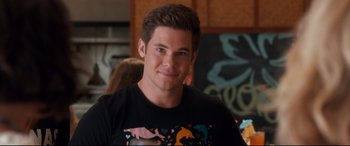 Movie still from “Mike and Dave Need Wedding Dates” (2016), directed by Jake Szymanski – A young man smiles for the camera in front of a wall; Close Up shot, Over the shoulder angle