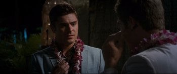 Movie still from “Mike and Dave Need Wedding Dates” (2016), directed by Jake Szymanski – A man in a suit and a flower lei; Close Up shot, Over the shoulder angle
