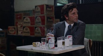 Movie still from “Mikey and Nicky” (1976), directed by Elaine May – A man sitting at a table smoking a cigarette and drinking milk; Medium shot, Over the shoulder angle