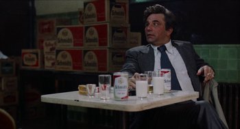 Movie still from “Mikey and Nicky” (1976), directed by Elaine May – A man sitting at a table in front of a bunch of boxes; Medium shot, Over the shoulder angle