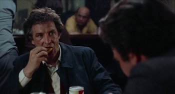Movie still from “Mikey and Nicky” (1976), directed by Elaine May – A man sitting at a table eating a donut; Close Up shot, Over the shoulder angle