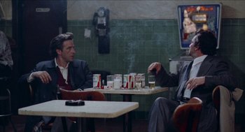 Movie still from “Mikey and Nicky” (1976), directed by Elaine May – Two men sitting at a table with drinks and cigarettes; Wide shot, Over the shoulder angle