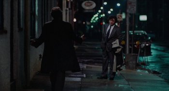 Movie still from “Mikey and Nicky” (1976), directed by Elaine May – A man wearing a suit and tie standing on a sidewalk; Wide shot, Over the shoulder angle